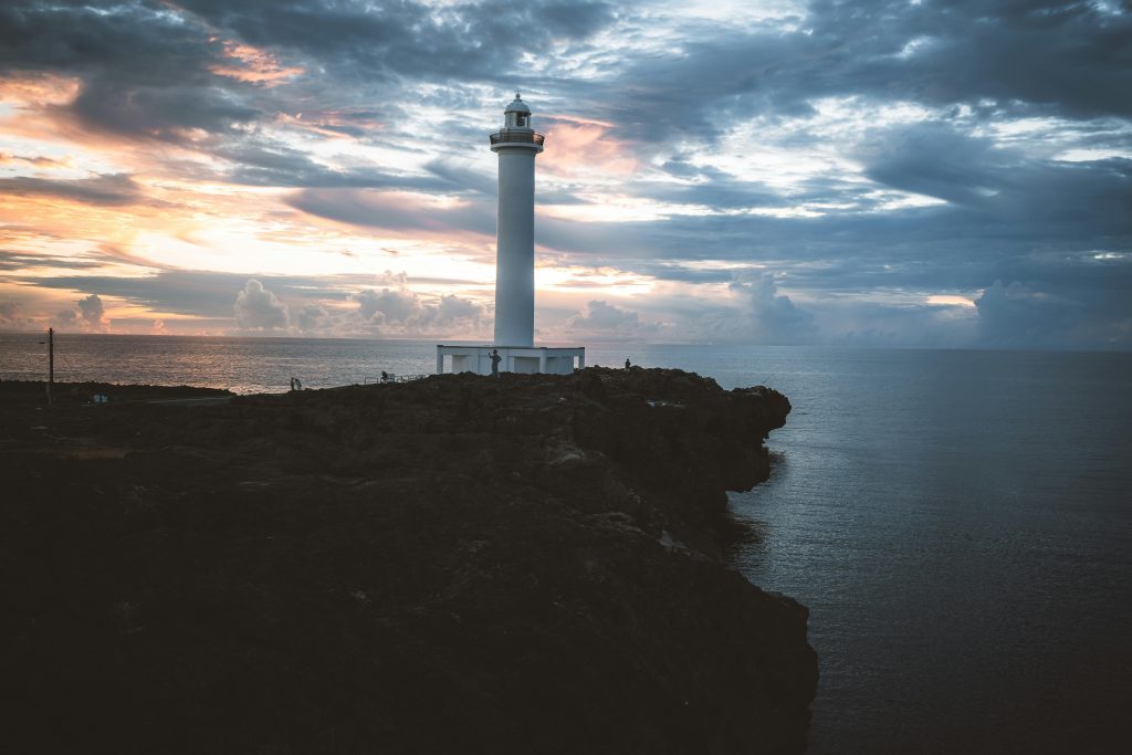 A tranquil view of a lighthouse by the sea during sunset on Okinawa's rugged coastline.